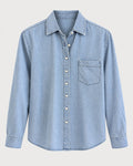 The Shirt Long Sleeve Boxy Crop by The Shirt is a light blue denim women’s cotton shirt featuring a button-down front with a no gape button, a single chest pocket on the left, and a classic collar, displayed against a plain background.