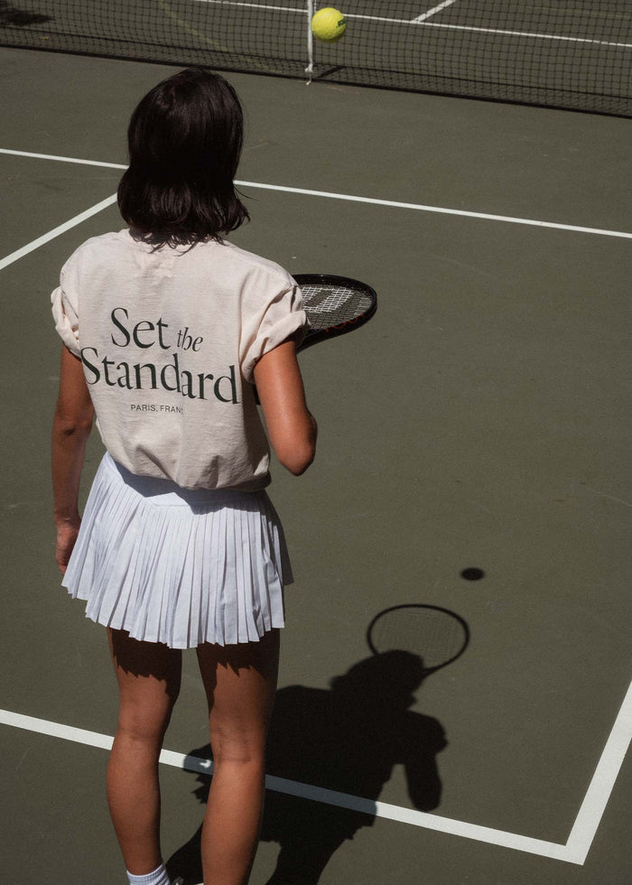 woman playing tennis on a court wearing a Kinn x Prince The Standard Tee and a white tennis skirt