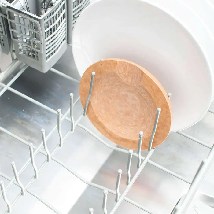 Top rack view of Natural Round tool rest seated between dishwasher tines with a white plate behind