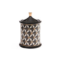 A cylindrical decorative container with a matching lid, featuring a black, white, and gold geometric pattern on the body and a solid black lid and base with a small gold finial on top, set against a plain white background.