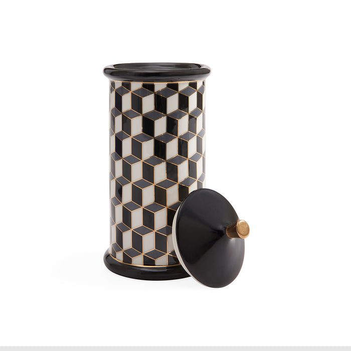 A cylindrical decorative container with a black and white geometric cube pattern and a matching black lid leaning against it on a white background.