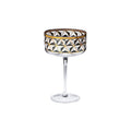 A clear stemmed coupe glass with a geometric faceted pattern in black, white, and gold on the bowl, set against a plain white background.