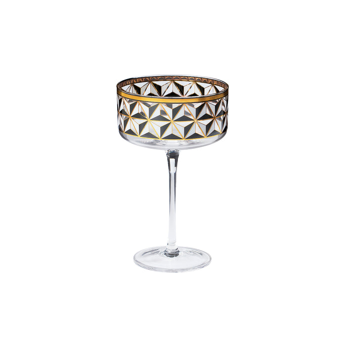 A clear stemmed coupe glass with a geometric faceted pattern in black, white, and gold on the bowl, set against a plain white background.