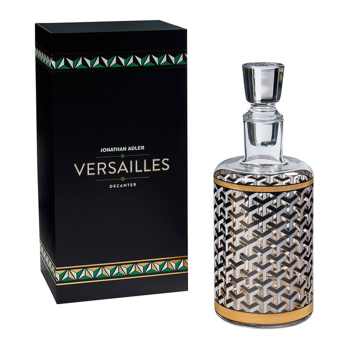 Jonathan Adler Versailles Decanter by Jonathan Adler, featuring a clear glass decanter with a black, white, and gold geometric pattern, shown next to its black presentation box with green and gold accents.