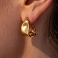 Close-up image of a gold indented unique shaped triangle hoop earring on a person's ear.
