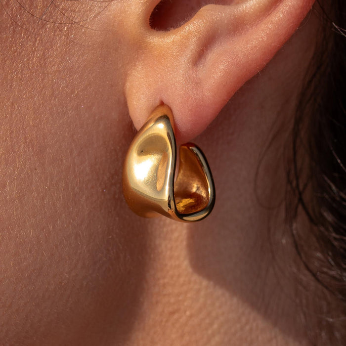 Close-up image of a gold indented unique shaped triangle hoop earring on a person's ear.
