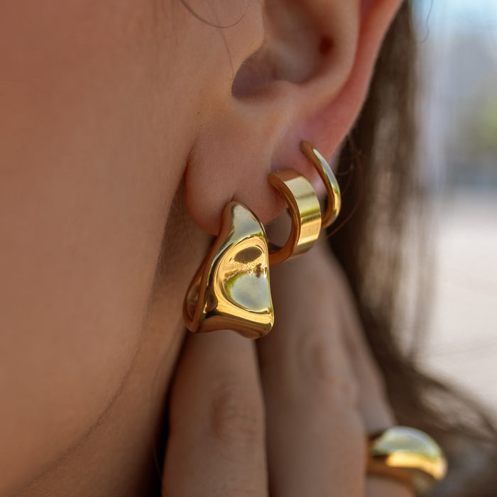 Gold earrings worn by a person with a blurred background