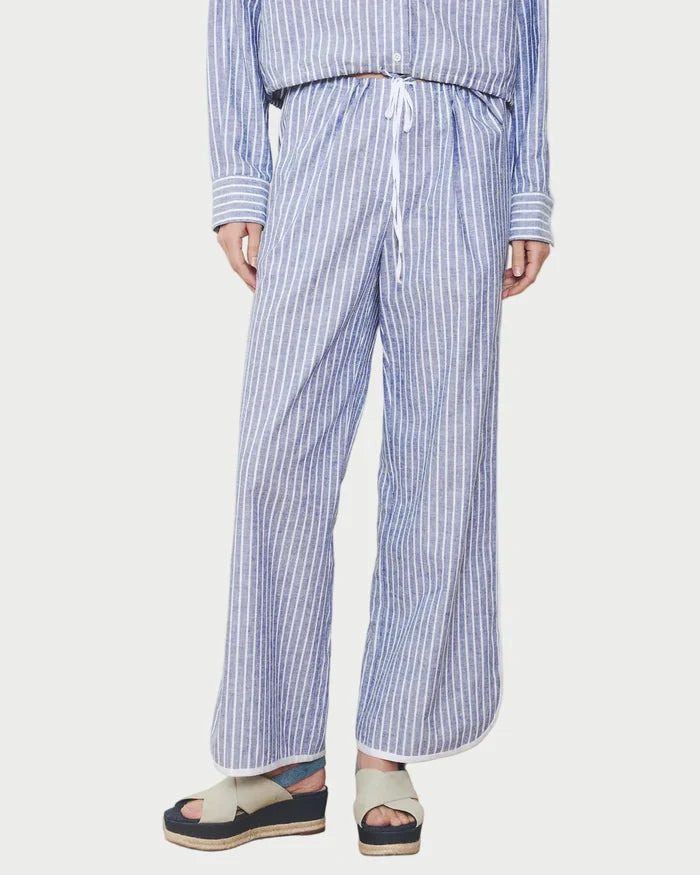 Person wearing a blue and white striped outfit with wide-leg pants against a white wall.