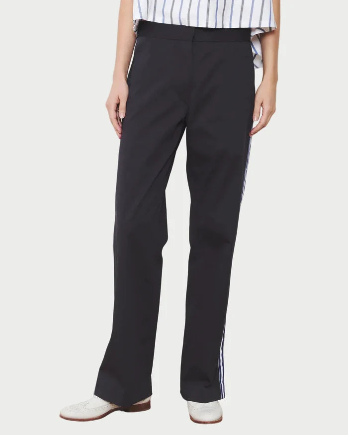 Person wearing navy pants with a white stripe on a wooden floor and white wall background