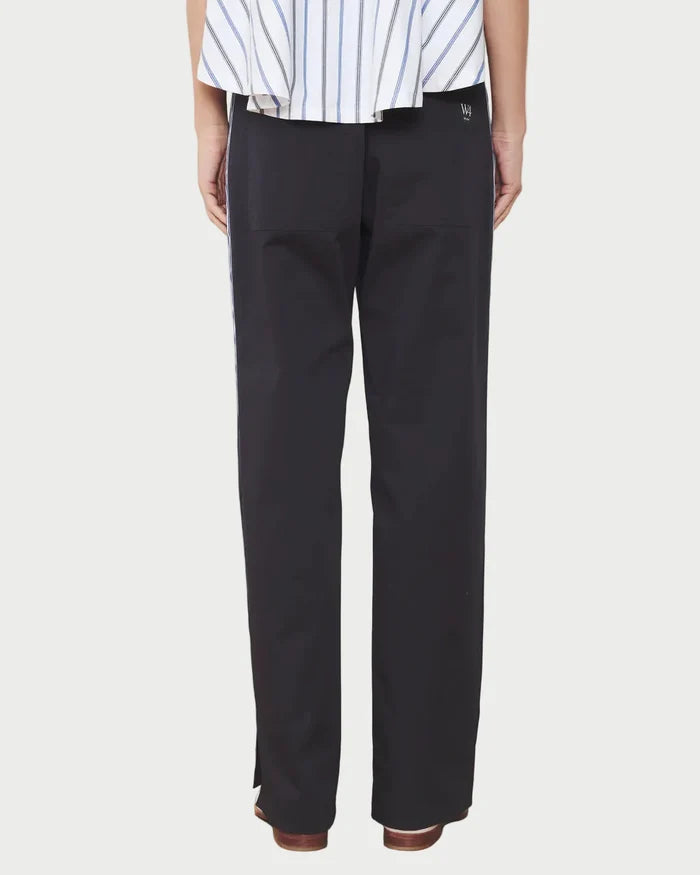 Person wearing navy pants and a striped shirt against a white wall.