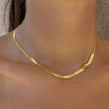 A close-up image of a person wearing a sleek gold choker necklace with a herringbone pattern.