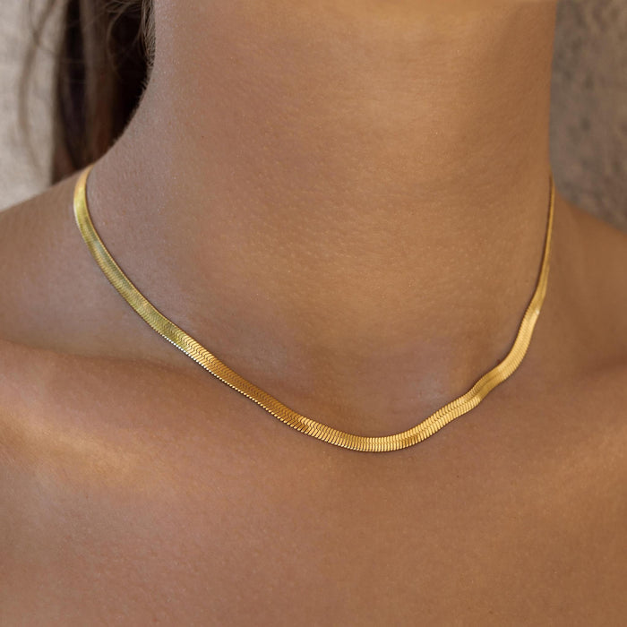 A close-up image of a person wearing a sleek gold choker necklace with a herringbone pattern.