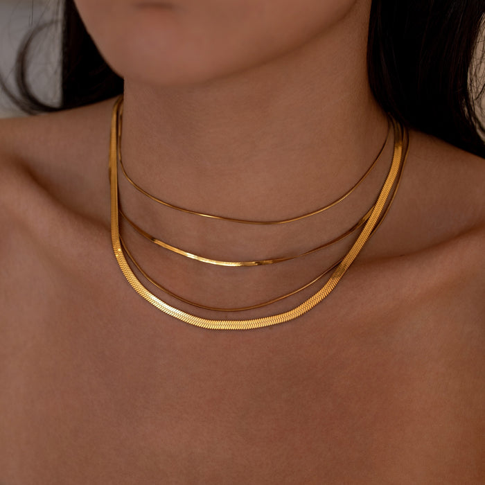 Close-up of a person wearing a simple everyday gold necklace stack with a neutral background