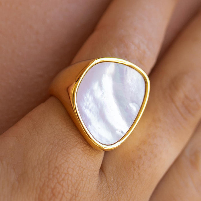 A waterproof gold ring with a large mother-of-pearl-like stone set on a person's finger.